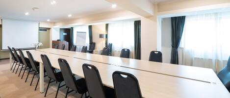 A conference room with a long table, chairs, a projector screen, and a whiteboard.