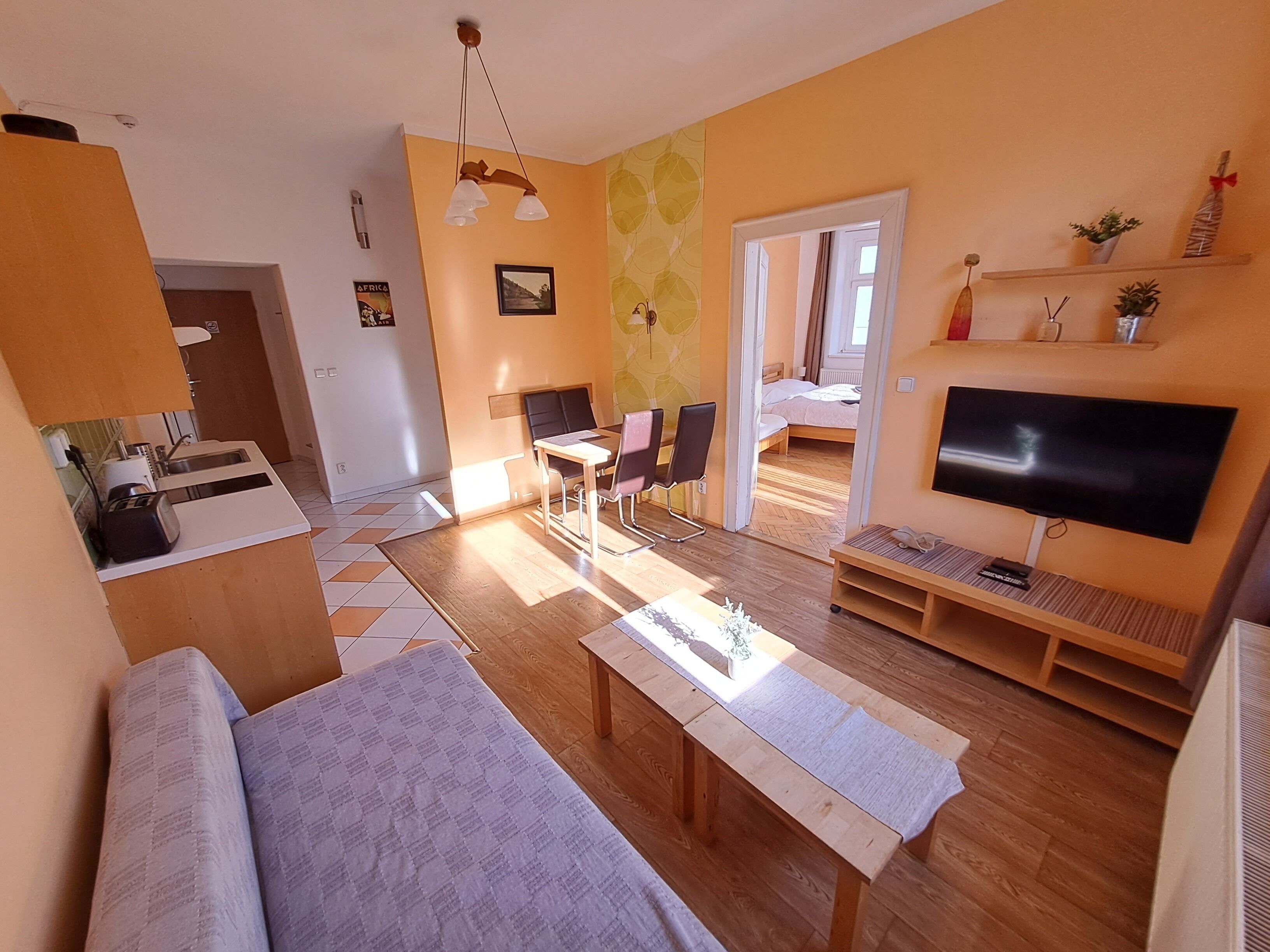 A modern living room with a sofa, coffee table, TV, and a dining area with chairs and a table.