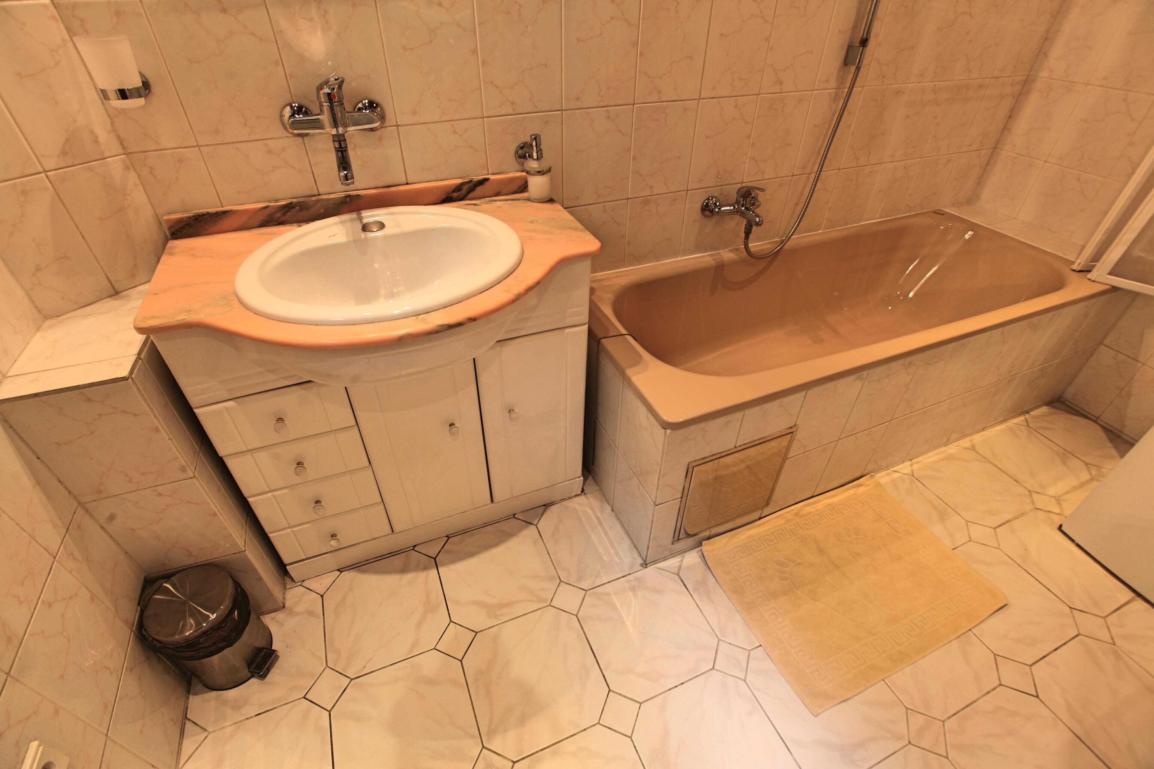 A bathroom with a marble sink, a bathtub, and a hexagonal tile floor.