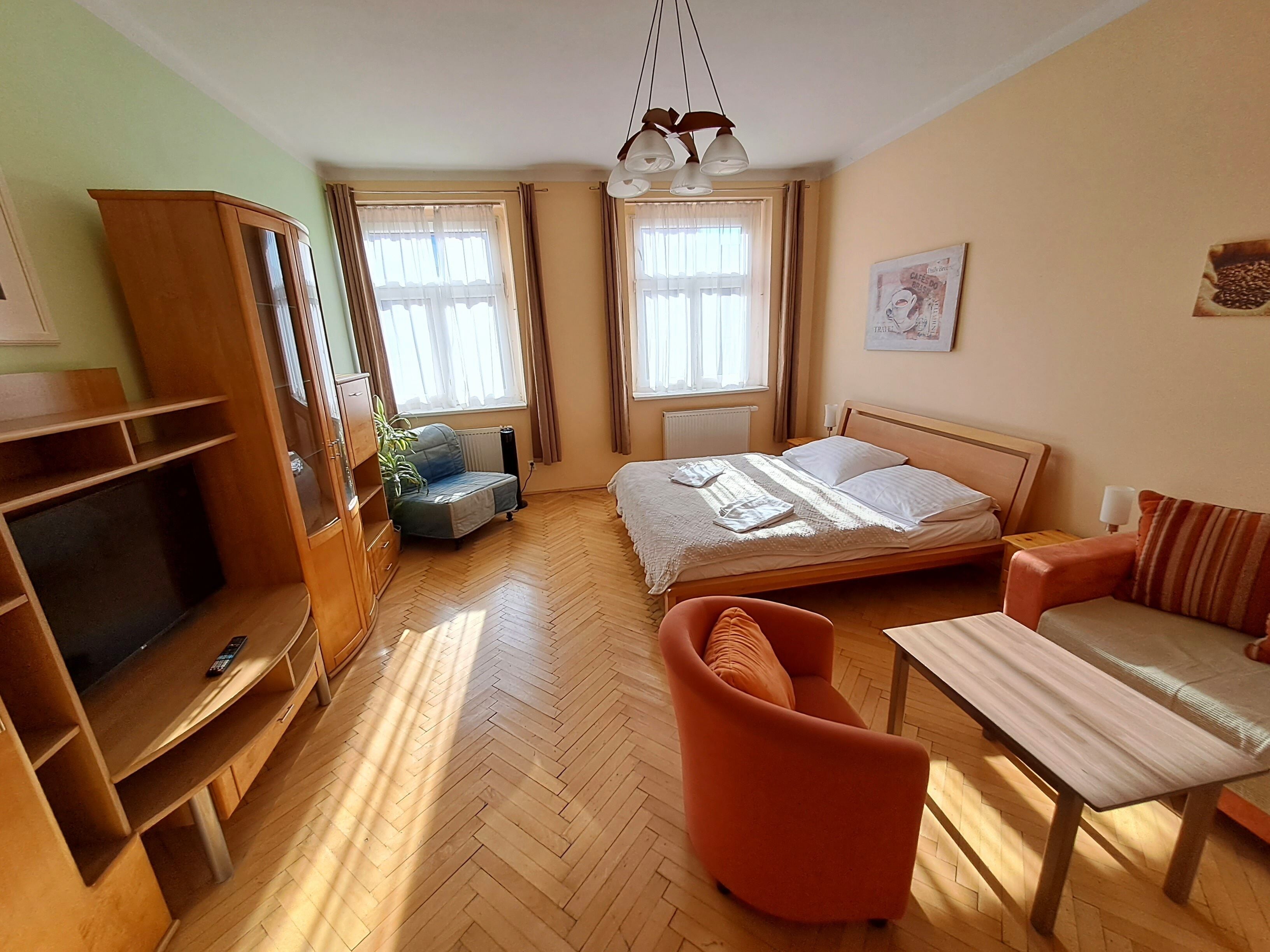 A hotel room with a bed, a TV, a desk, a chair, and a window with curtains.