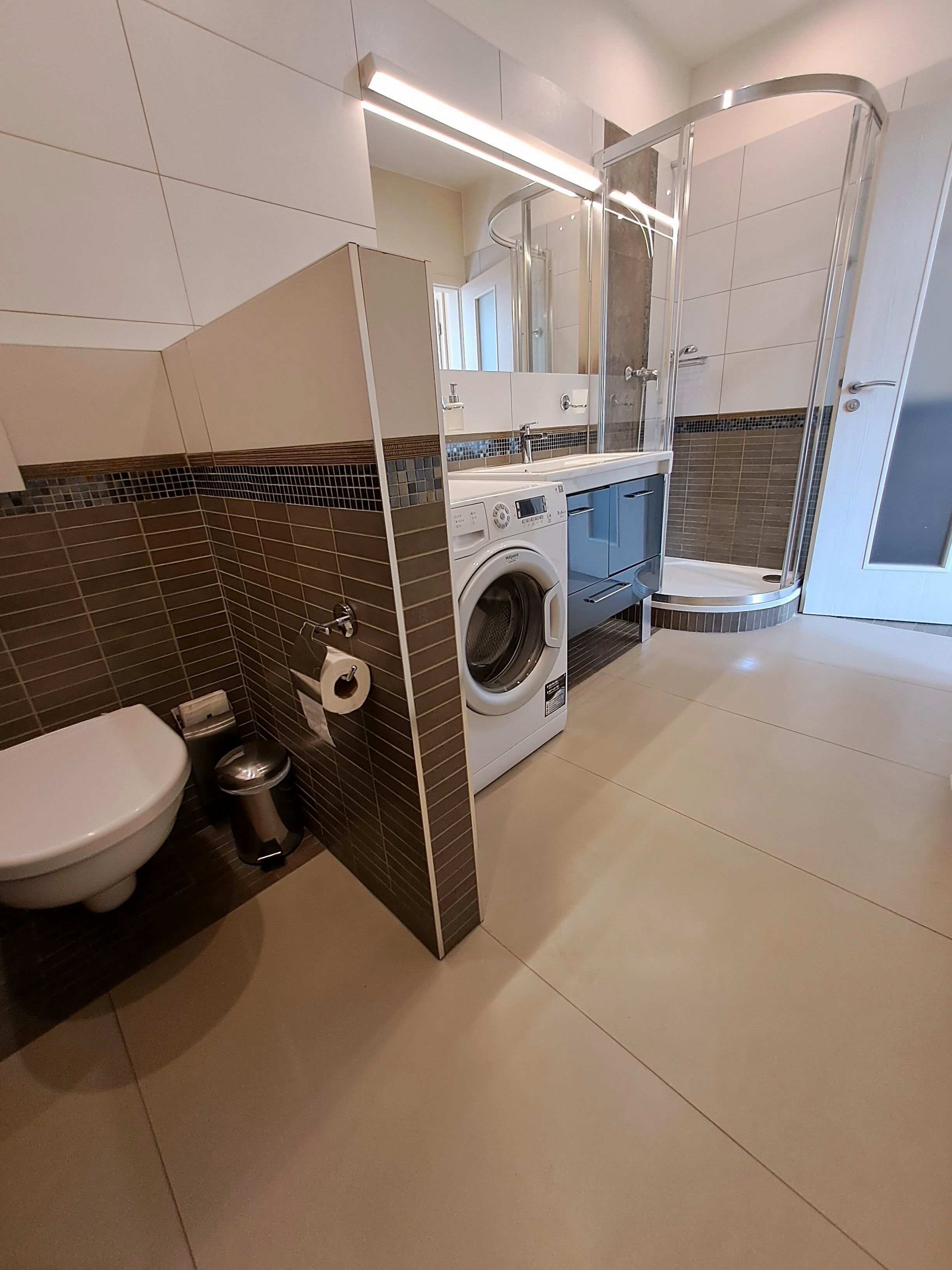 A modern bathroom with a toilet, washing machine, and shower.
