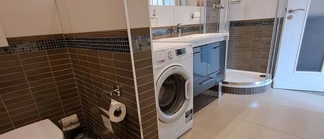 A modern bathroom with a toilet, washing machine, and shower.