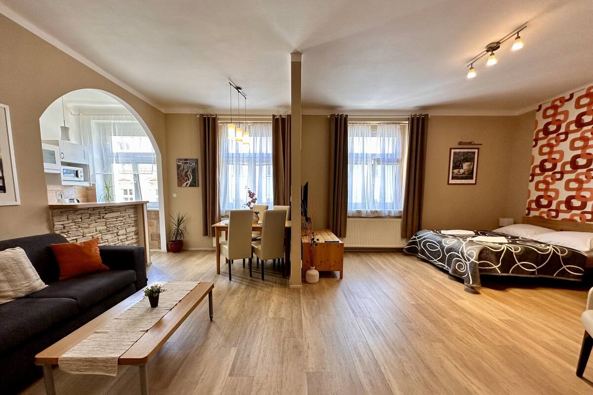 A modern living room with a sofa, dining table, and a bed. There is a kitchen area in the background.