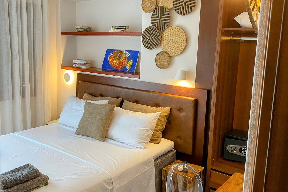 A neatly made bed with a wooden headboard, a bedside table with a lamp, and a wall decorated with circular woven art pieces.