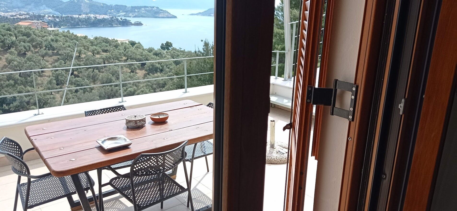 Un balcon avec une table et des chaises en bois, offrant une vue panoramique sur une zone côtière, avec des arbres et des bâtiments.
