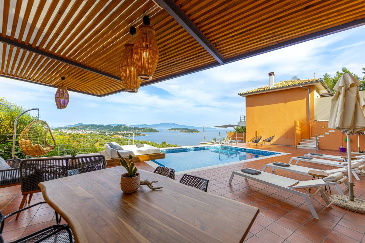 A poolside area with a wooden table, lounge chairs, and a view of the sea.