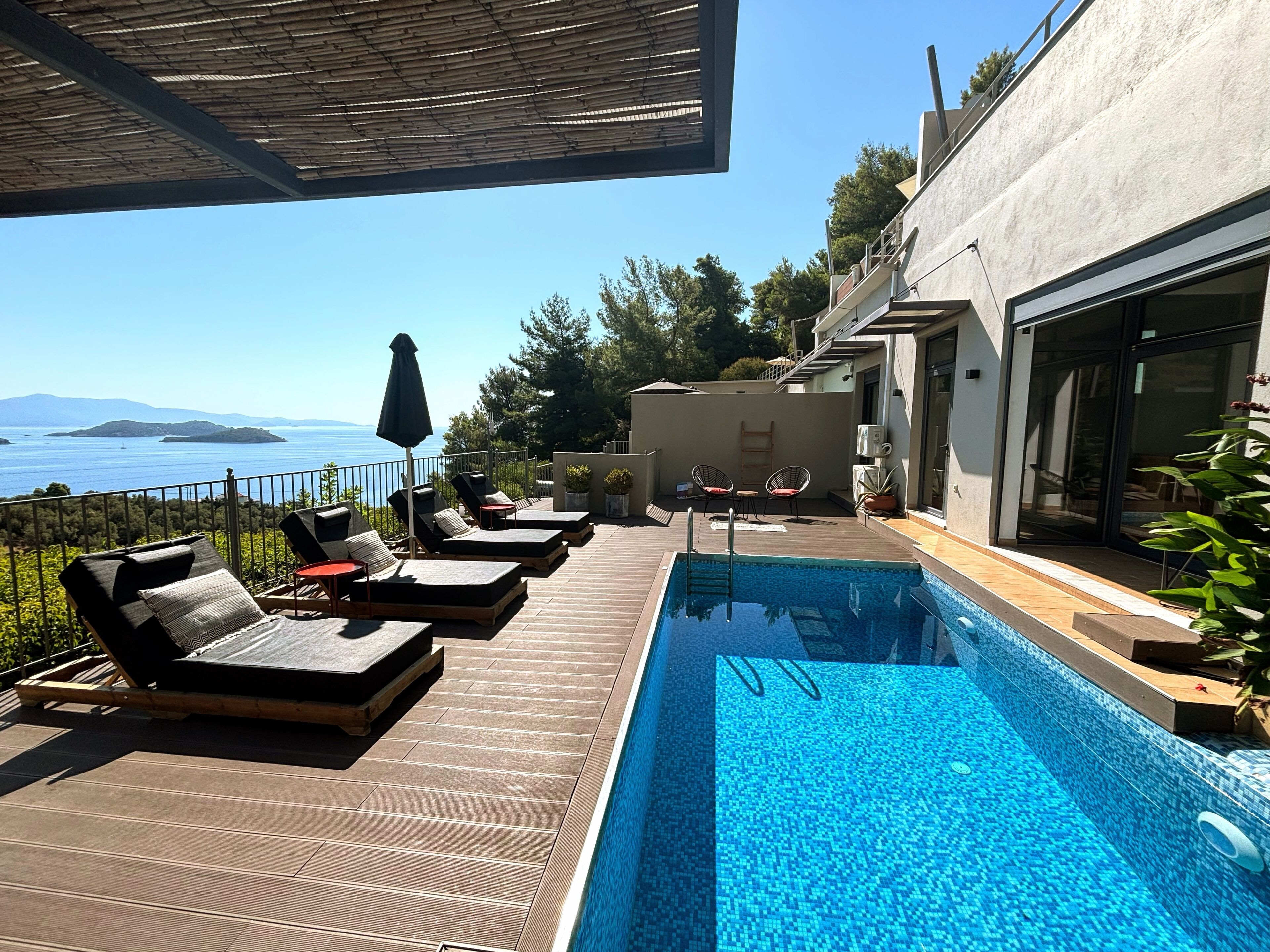 A poolside area with lounge chairs, a small table, and a view of the sea.