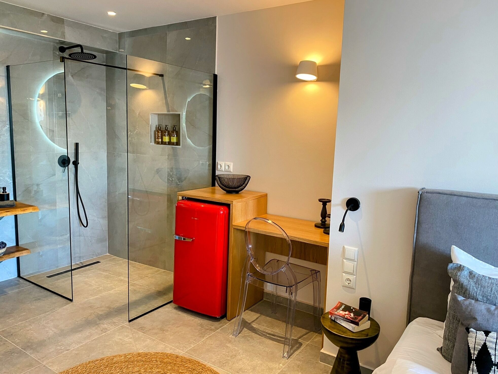 A modern bathroom with a glass-enclosed shower, a red refrigerator, and a wooden desk with a chair.