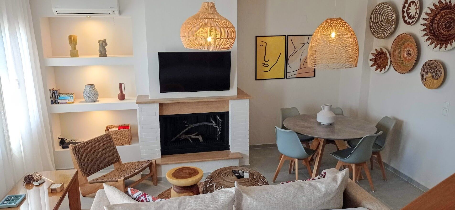 A living room with a fireplace, a television, wicker furniture, and decorative wall art.