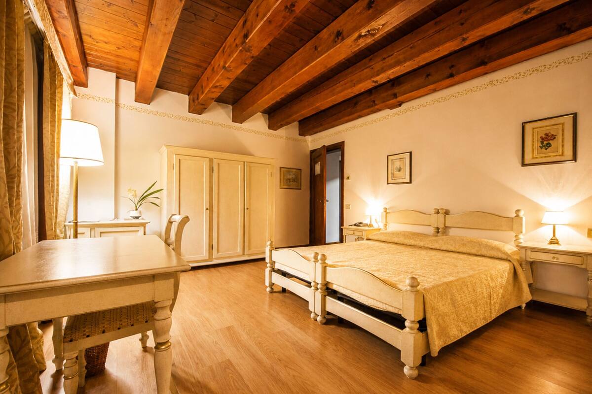 Une chambre avec un plafond en bois, un lit avec une tête de lit, une table de chevet, une commode, un bureau, une chaise, une armoire et une lampe.