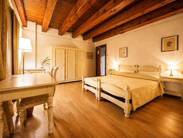 A bedroom with a wooden ceiling, a bed with a headboard, a bedside table, a nightstand, a desk, a chair, a wardrobe, and a lamp.