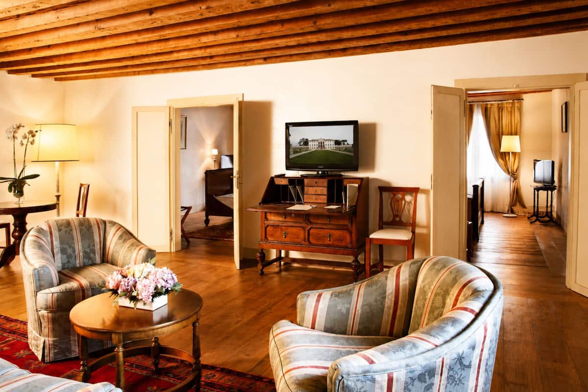 Une pièce avec un plafond en bois, un téléviseur posé sur un meuble en bois, un canapé, un fauteuil et une table agrémentée de fleurs.