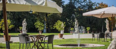 Een terras met tafels en stoelen, parasols en een fontein.