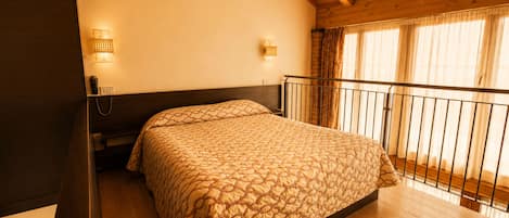 Un dormitorio con techo de madera, una cama con colcha estampada, una mesita de noche con lámpara y una ventana con cortinas.