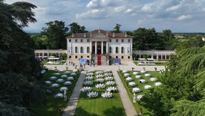 A grand building with a symmetrical facade, a central entrance with columns, and a formal garden with neatly arranged tables and chairs.
