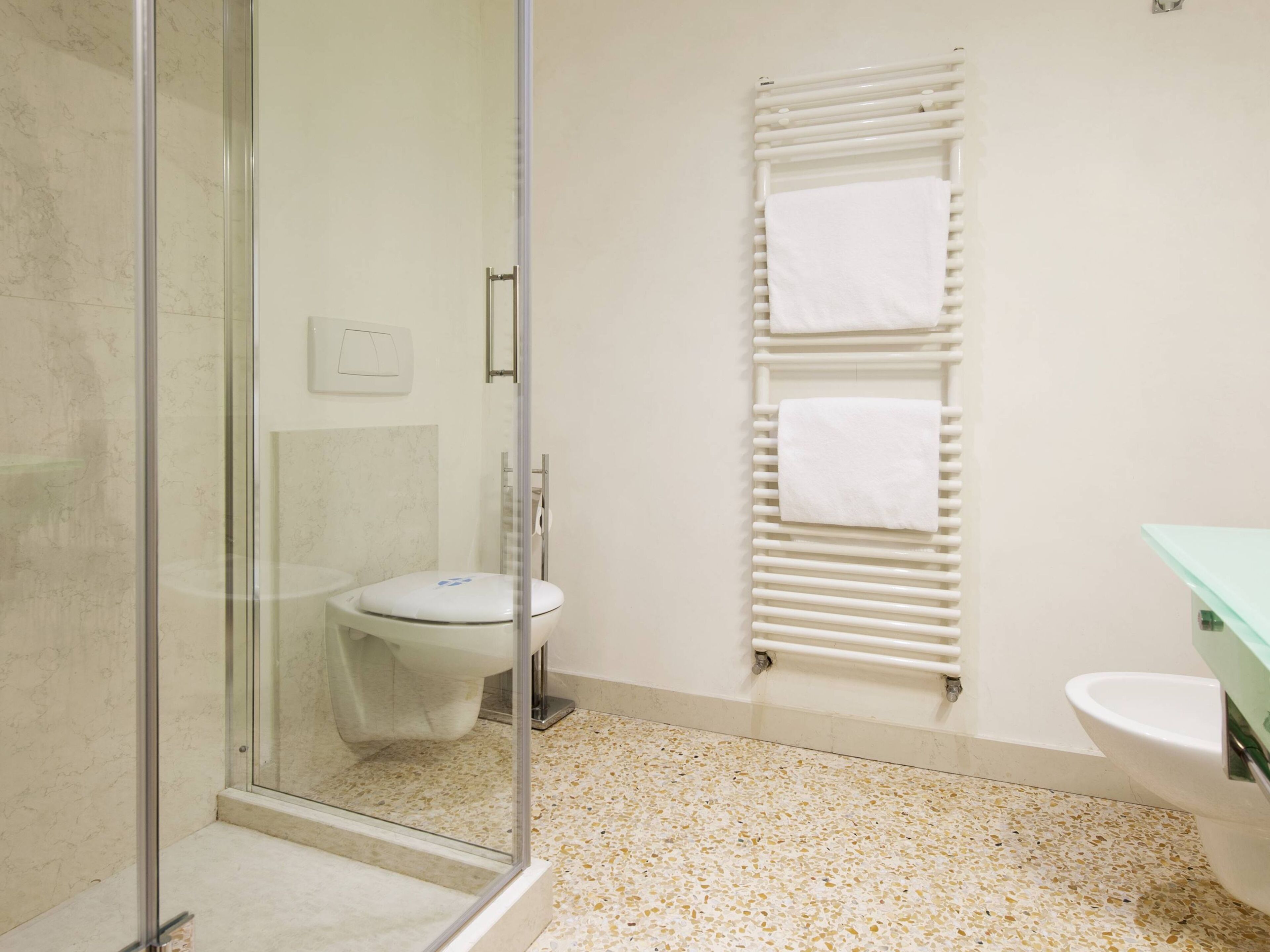 Un baño con cabina de ducha de vidrio, inodoro, toallero blanco y lavabo con encimera verde.