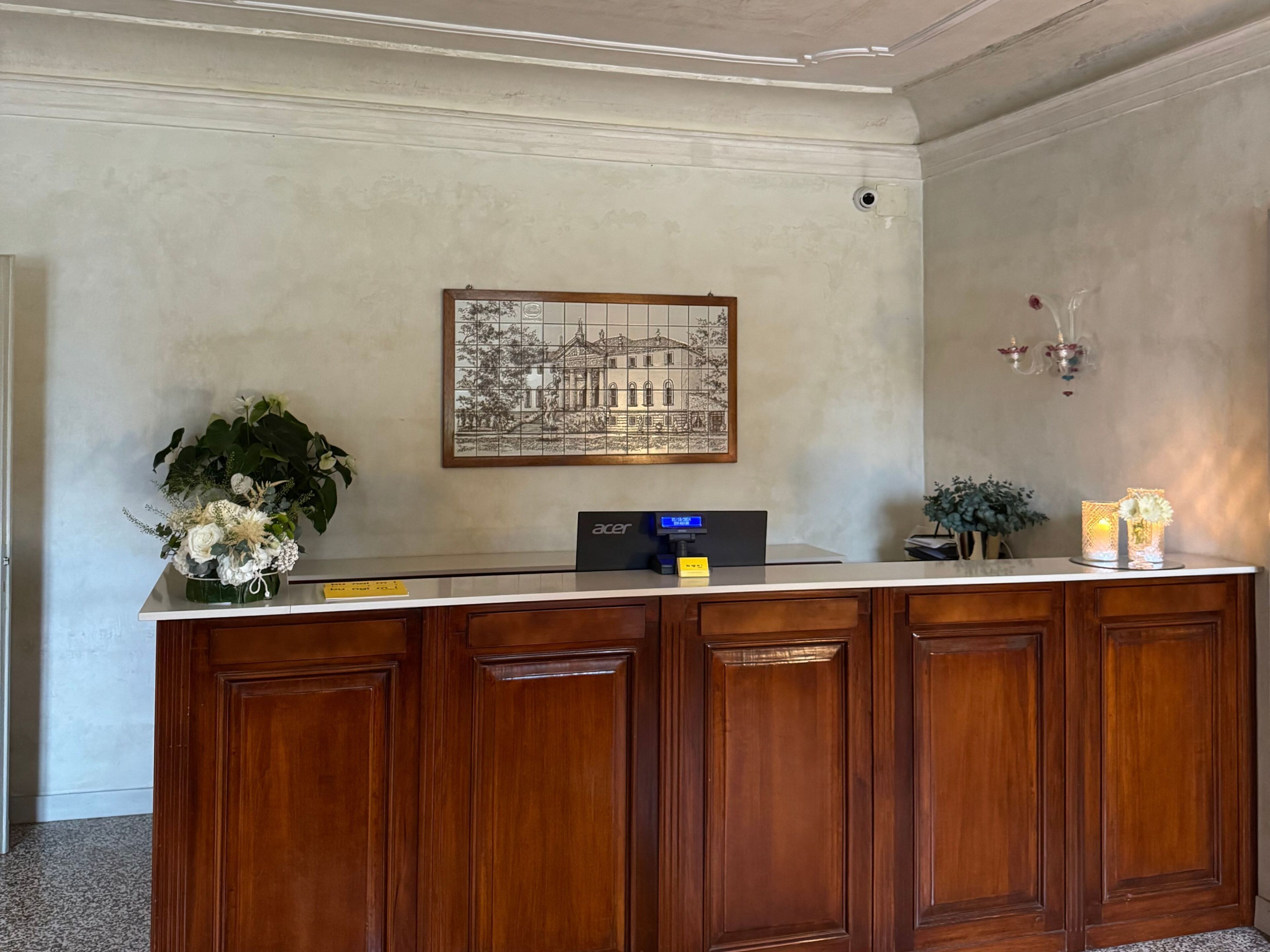 A reception desk with a framed architectural drawing, a digital display, and a potted plant.