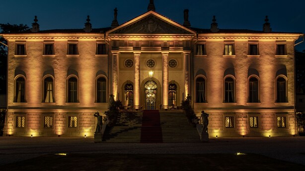 A large, classical building with a grand entrance, multiple windows, and a central staircase leading to the main doors.