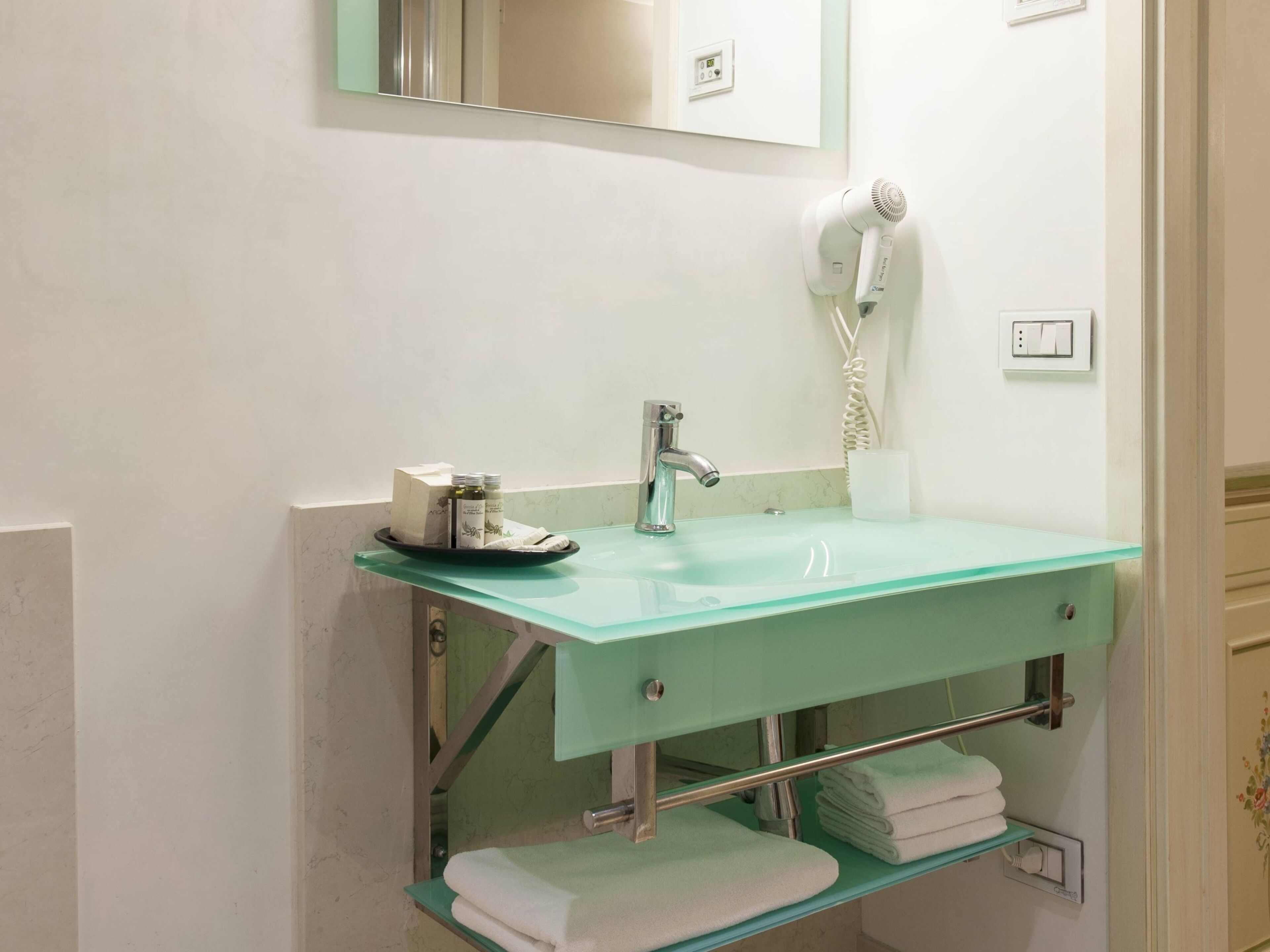 Un bagno con lavabo in vetro, uno specchio, un asciugacapelli e un porta asciugamani.