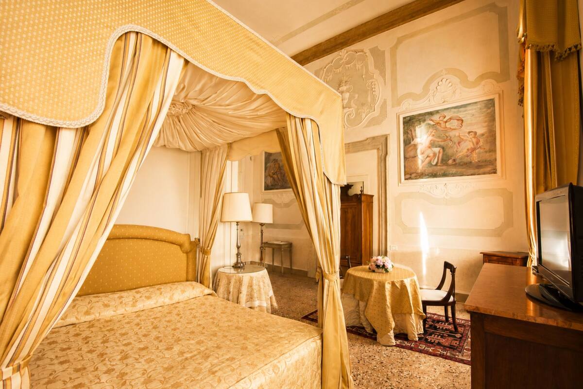 Un lit à baldaquin, une télévision, une petite table ronde avec une lampe et une chaise, le tout dans une pièce aux murs richement décorés.