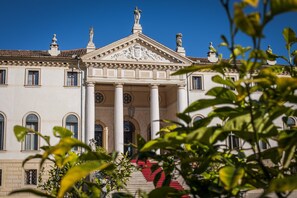 Stately building with a central entrance, flanked by columns, surrounded by lush greenery.