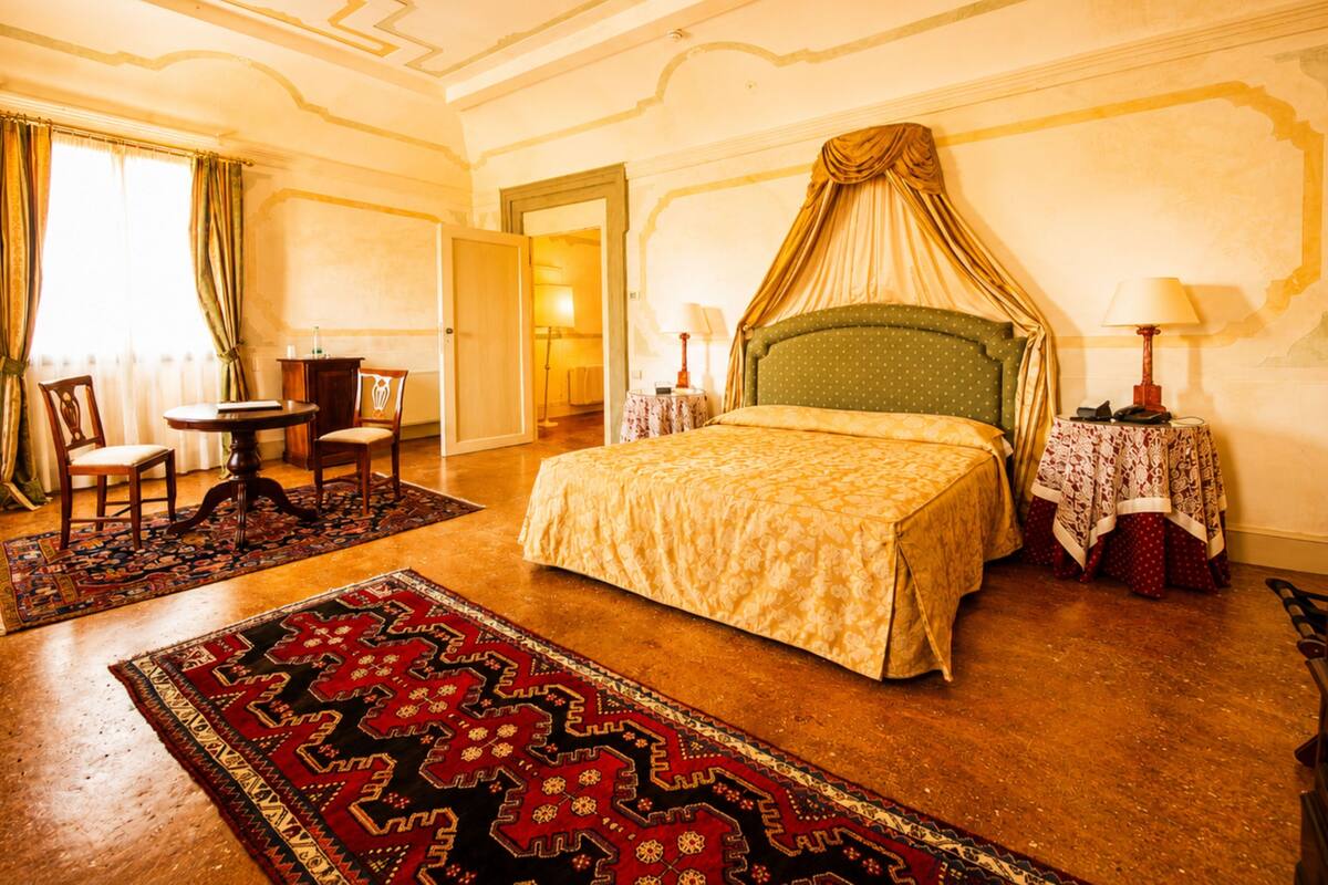 Une chambre avec un lit à baldaquin, une petite table avec des chaises, une lampe et un tapis à motifs.