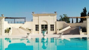 A pool with a clear blue water surface, surrounded by a white building with a grand entrance and steps leading up to it.