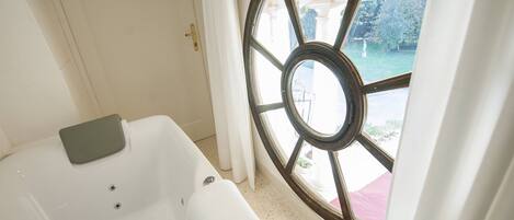 Ein Badezimmer mit Badewanne, einem Fenster mit Gartenblick und einer Tür.