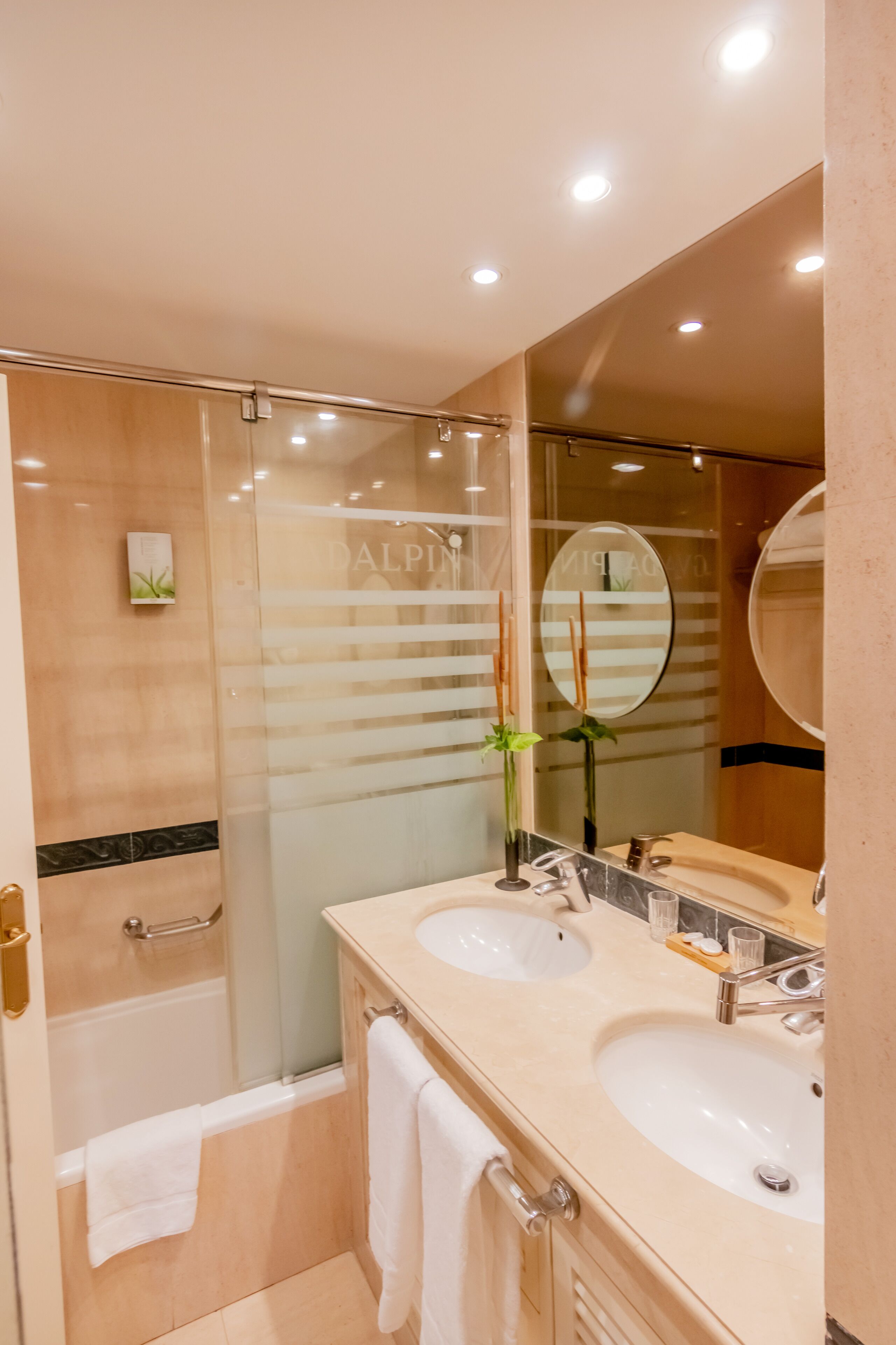 A modern bathroom with two sinks, a glass shower enclosure, and a large mirror.