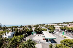 Eine Tankstelle mit grünem Vordach, umgeben von Bäumen und Gebäuden, mit freiem Blick auf das Meer im Hintergrund.