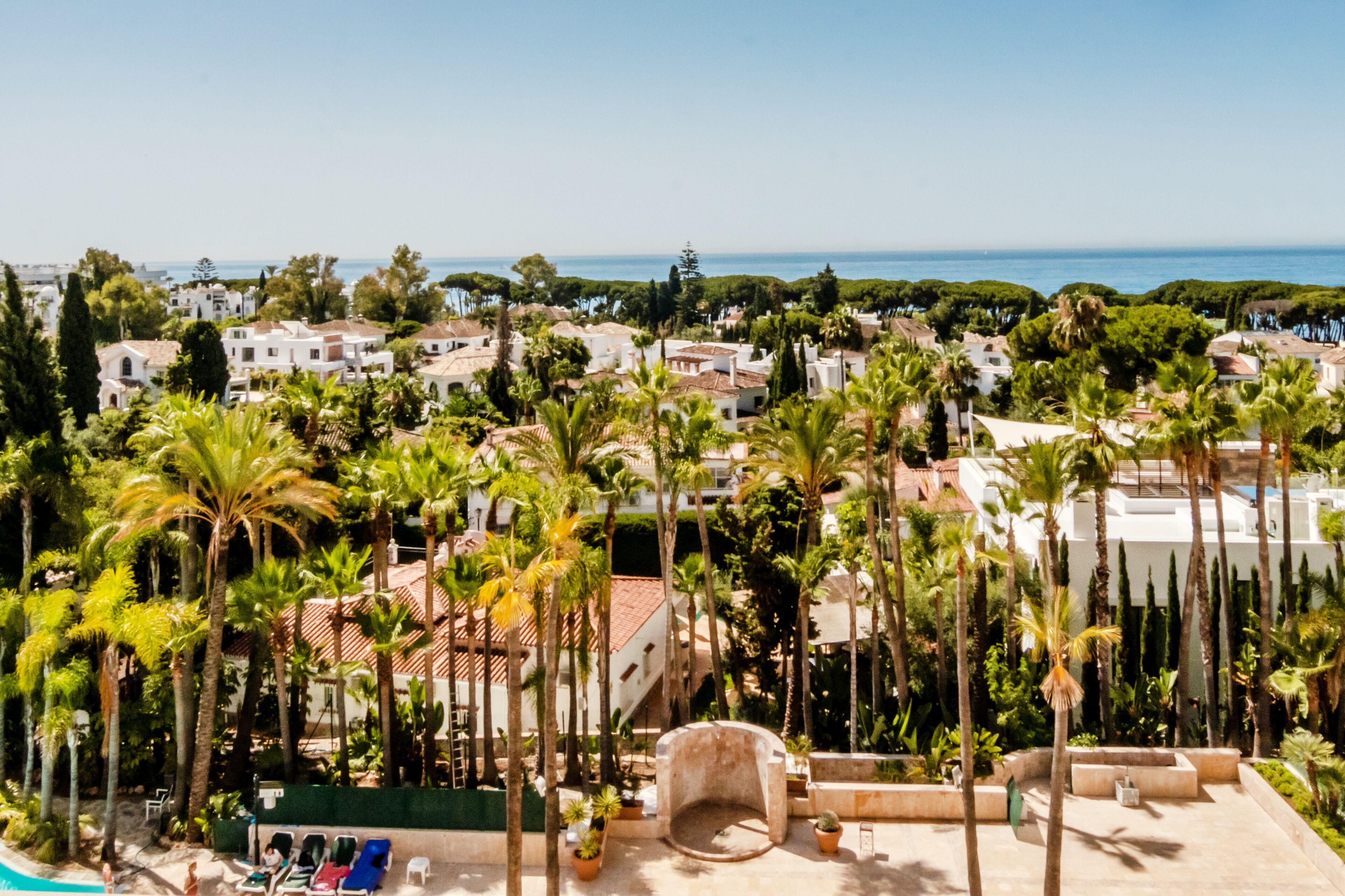 Um resort com área de piscina rodeada por palmeiras e vista para o mar.