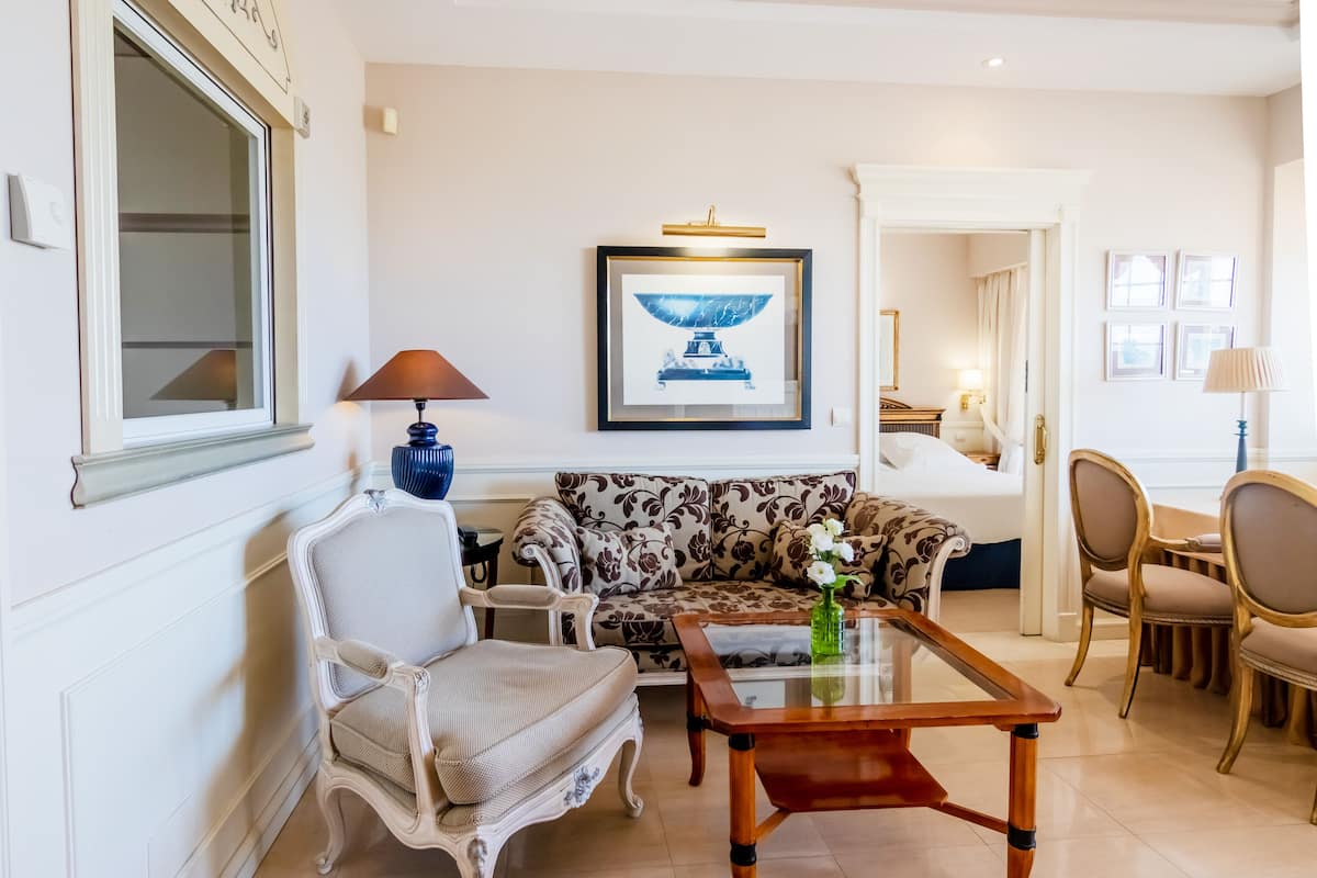 A living room with a patterned sofa, a wooden coffee table, a white armchair, and a framed artwork on the wall.