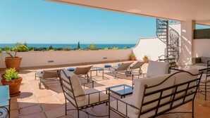 A terrace with outdoor seating, potted plants, and a spiral staircase. - Guadalpin Suites (Marbella)