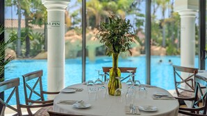 A dining table set for six with a vase of flowers, a pool view, and a white tablecloth. - Guadalpin Suites (Marbella)