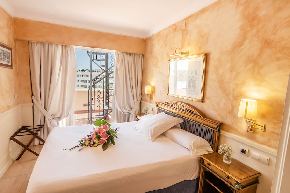 A hotel room with a bed, a nightstand, a mirror, and a window with curtains.