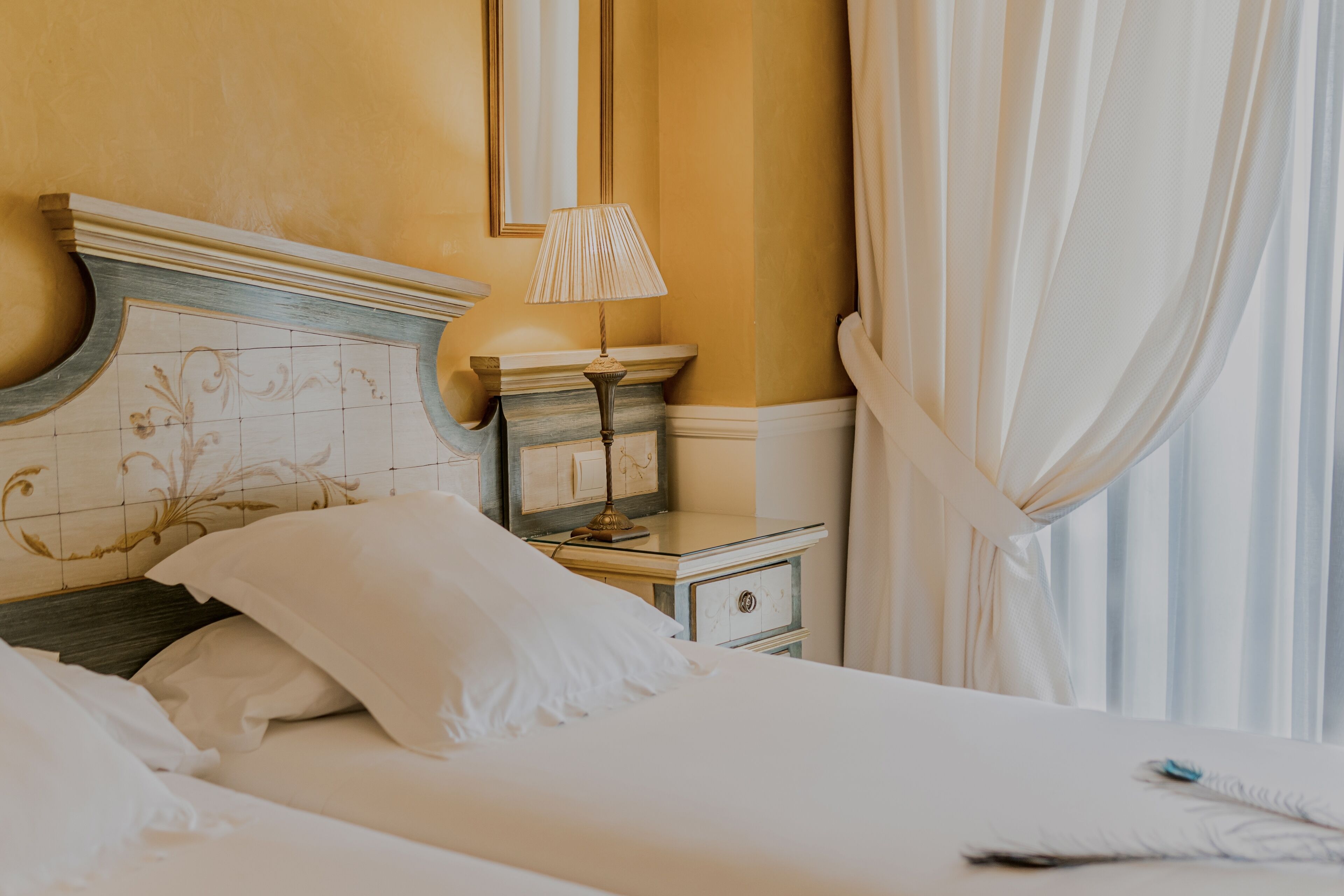 Habitación de hotel con cama, mesita de noche, lámpara y espejo.