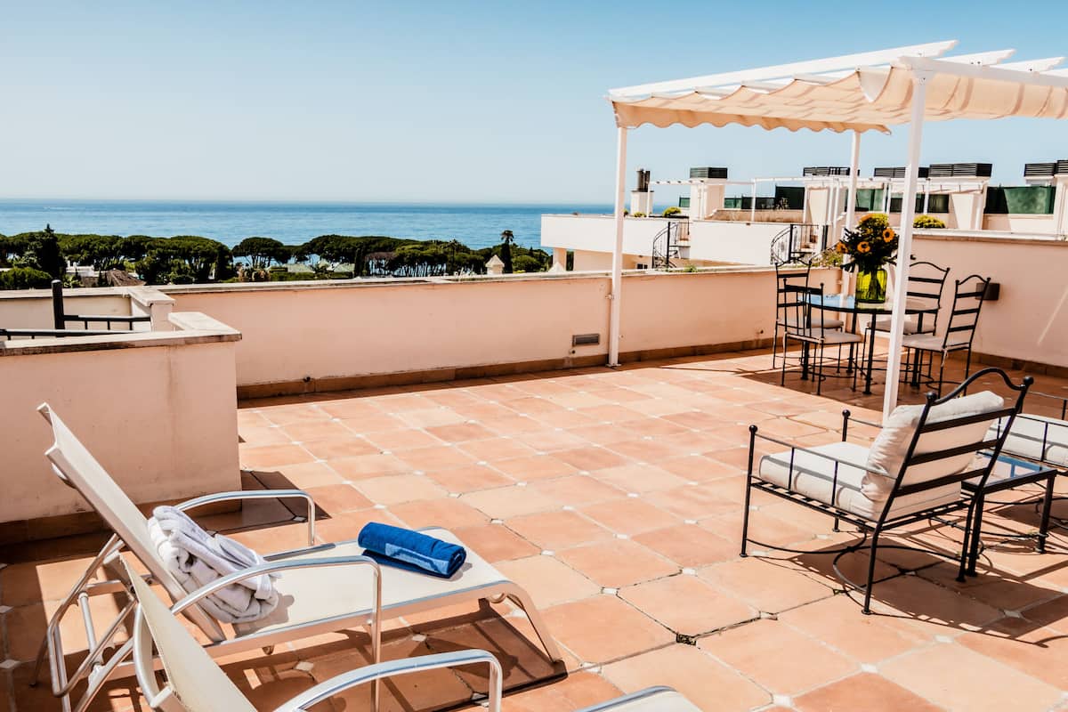 A rooftop terrace with a view of the sea, featuring lounge chairs, a table with chairs, and a pergola.