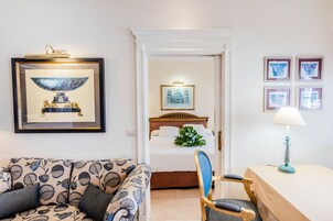 A hotel room with a bed, a sofa, a chair, a table with a lamp, and framed artwork on the walls.