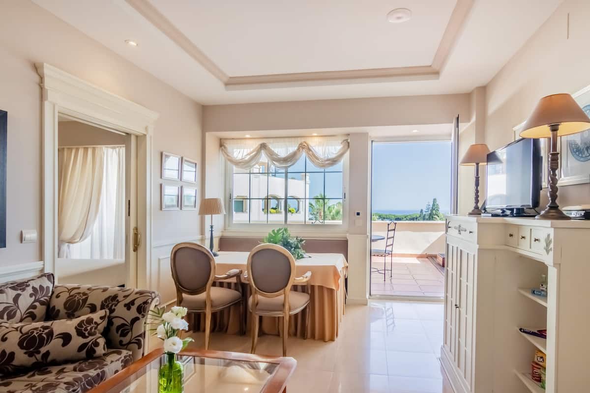 A spacious living area with a sofa, dining table, chairs, and a view of the outdoors.
