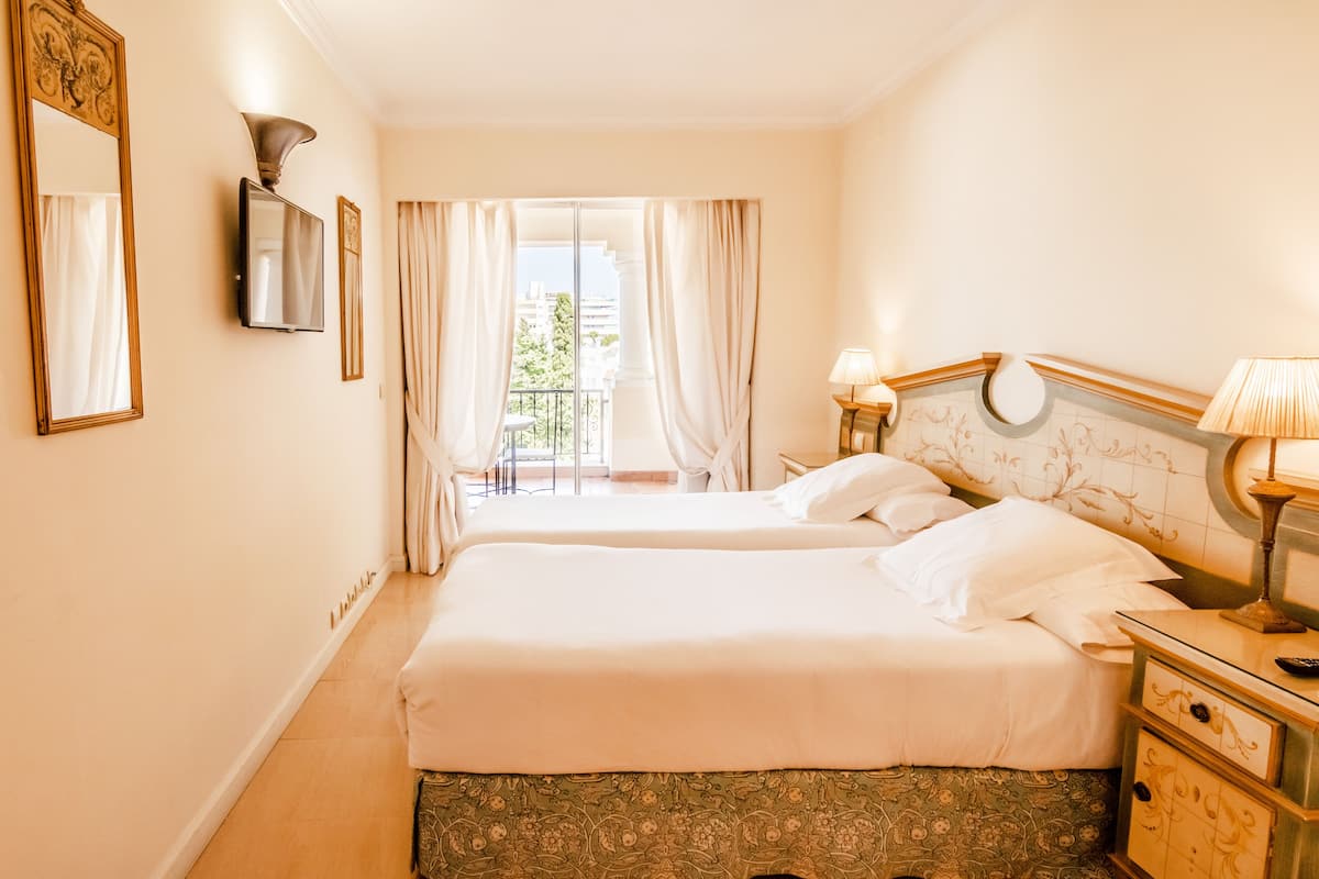 A hotel room with two beds, a TV, a lamp, and a view of the outdoors.