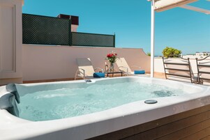 Ein Whirlpool mit Holzterrasse, zwei Liegestühle und ein Tisch mit Blumenvase.