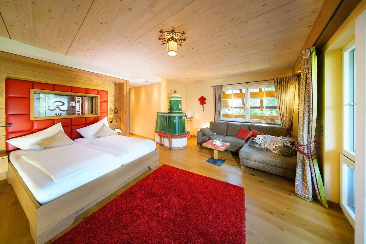 Ein Zimmer mit einem Bett, einem Sofa, einem roten Teppich, einem grünen Dekorationsobjekt und einem Fenster mit Vorhängen.