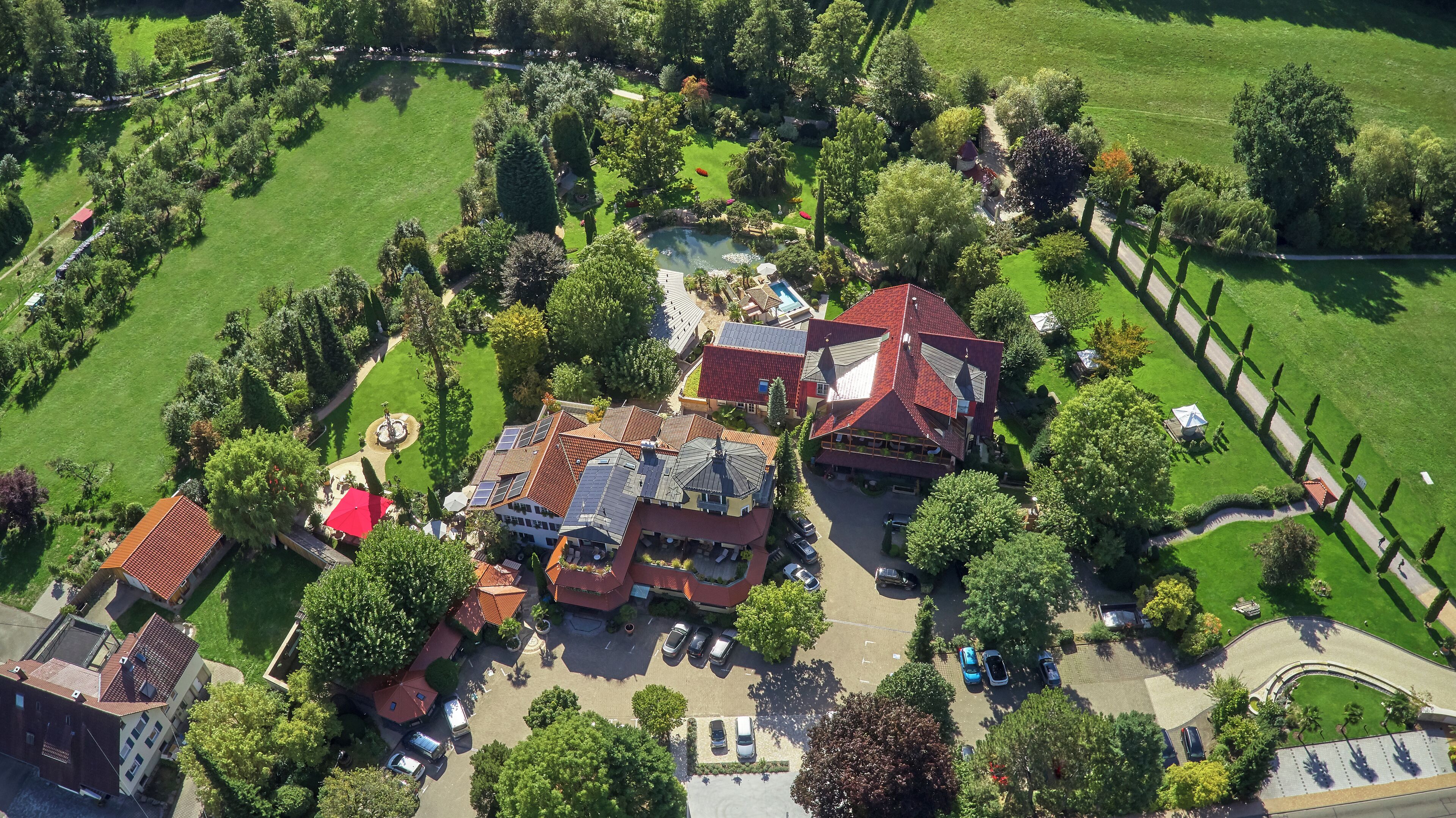 Eine Vogelperspektive eines Wohngebiets mit mehreren Häusern, einem zentralen Innenhof mit einem Brunnen und einem Schwimmbecken.