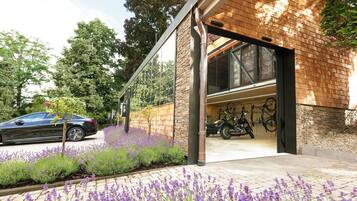 En moderne bygning med garage, en parkeret bil og en række lilla blomster i forgrunden.