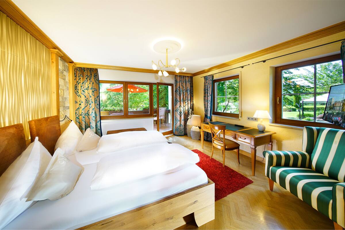 Ein Hotelzimmer mit einem großen Bett, einem Schreibtisch, einem Sessel und Blick ins Freie.