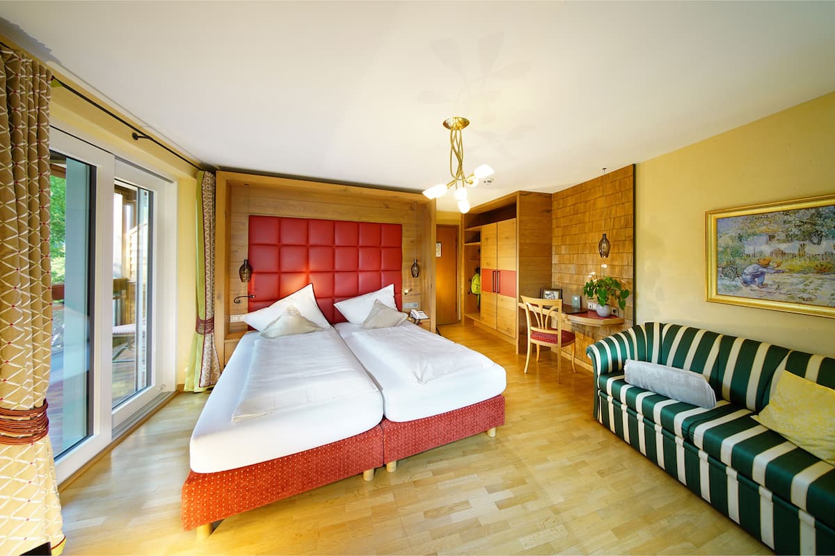 Ein Hotelzimmer mit einem großen Bett, einem grün gestreiften Sofa, einem Schreibtisch mit Stuhl und einem großen Fenster mit Vorhängen.