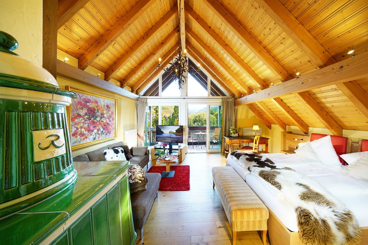 Ein geräumiges Zimmer mit hoher Holzbalkendecke, einem großen Bett mit weißer und brauner Bettwäsche, einem grünen Schrank und einem Bild an der Wand.