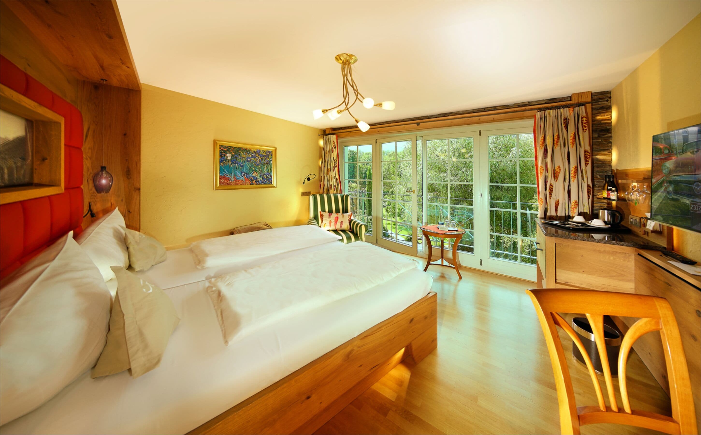 Un dormitorio con cama doble, cabecera de madera, un cuadro, una ventana con cortinas y vistas a zonas verdes.