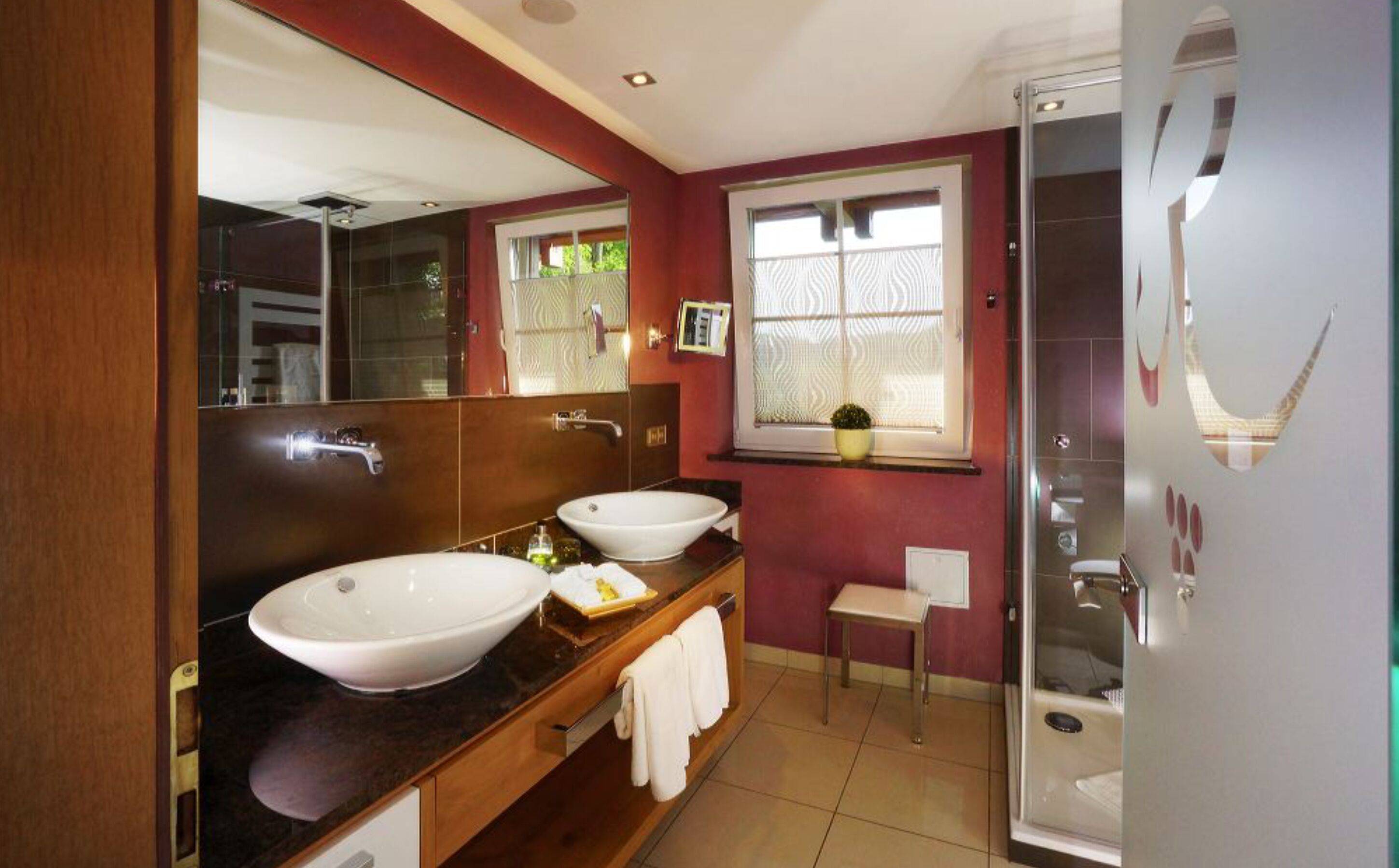 Ein modernes Badezimmer mit zwei Waschbecken, einem großen Spiegel, einem Fenster mit Blick und einer Duschkabine aus Glas.