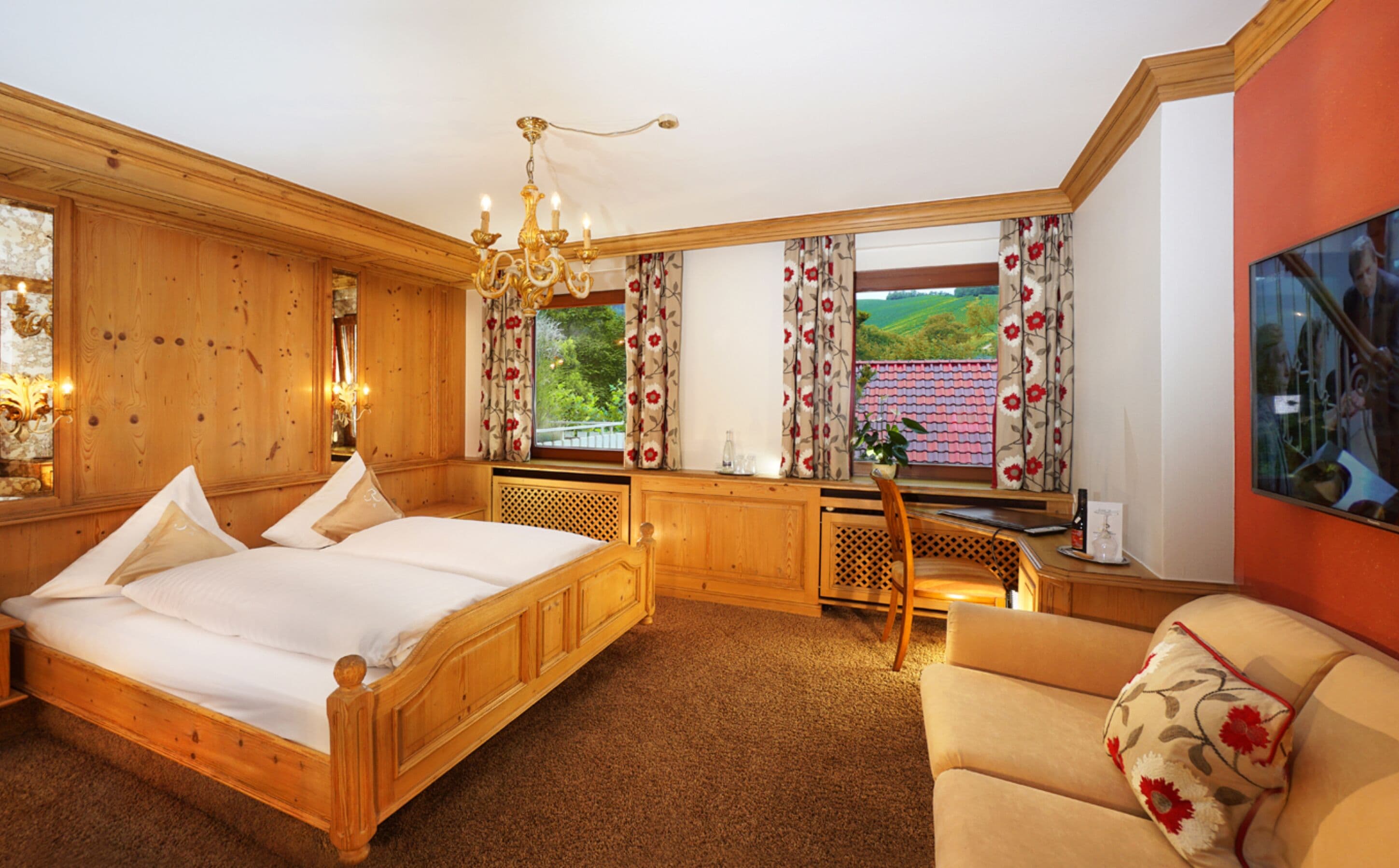 Ein Schlafzimmer mit einem hölzernen Bett, einem Schreibtisch, einem Stuhl und Blick auf einen Garten durch das Fenster.